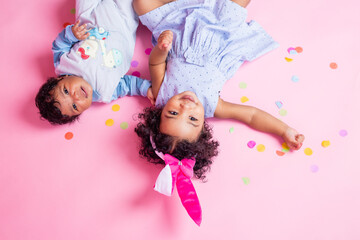 Obraz na płótnie Canvas two charming little girls with dark skin and curly hair in beautiful dresses are lying on the floor in confetti