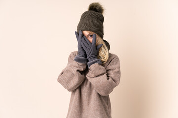 Young woman with winter hat over isolated background covering eyes and looking through fingers