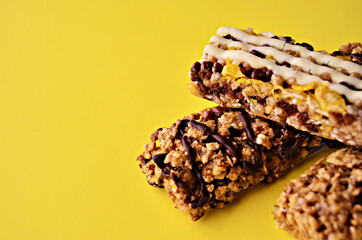 Three granola bars lie on top of each other on a yellow background looking side close-up from the left-facing space. High quality photo