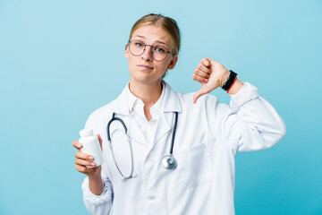 Fototapeta premium Young russian doctor woman holding pills bottle on blue showing a dislike gesture, thumbs down. Disagreement concept.