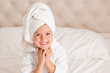 Fototapeta na wymiar little smiling girl in a white robe with a white towel on her head is lying in bed. portrait of a child