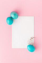 Easter composition. Easter blue eggs, feather and blank paper on pastel pink background. Flat lay, top view, copy space.