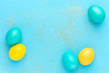 Minimalist Easter composition. Colorful easter eggs and glitter on pastel aquamarine background. Top view, copy space.