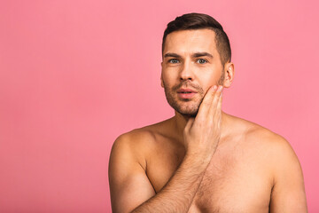 Fototapeta premium Photo of smiling young beautiful man standing isolated over pink wall background naked. Man's skincare concept in a bathroom.