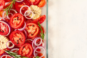 Top view of sliced tomatoes, garlic, onion, and rosemary in a glass oven dish. Mediterranean food....