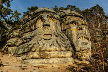 Fototapeta na wymiar Two giant heads of devils carved into sandstone rocks,each is about 9m high.Devils Heads created by Vaclav Levy near Libechov, Czech republic.Cliff carvings carved in pine forest.Tourist attraction.
