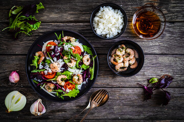 Prawn salad with white rice, lettuce, cherry tomatoes and onion on wooden background