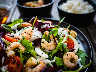 Prawn salad with white rice, lettuce, cherry tomatoes and onion on wooden background