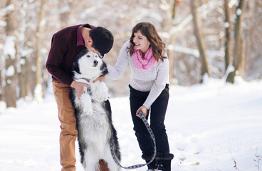 Attractive couple smiling and having fun in winter park with their husky dog