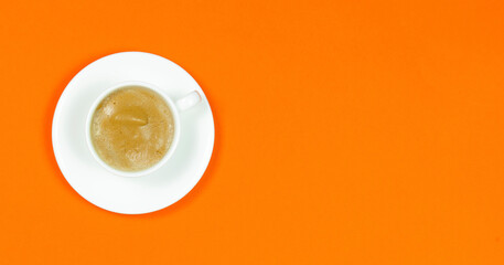 White cup with cappuccino and saucer on an orange background.