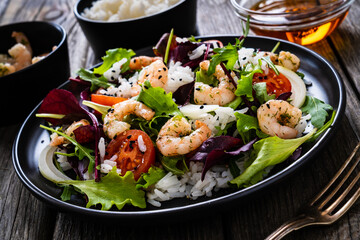 Prawn salad with white rice, lettuce, cherry tomatoes and onion on wooden background