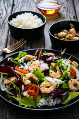 Prawn salad with white rice, lettuce, cherry tomatoes and onion on wooden background