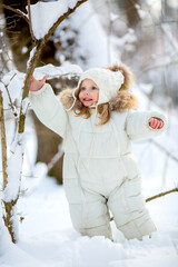 cute little girl in white winter clothes and a knitted hat walks in the winter forest