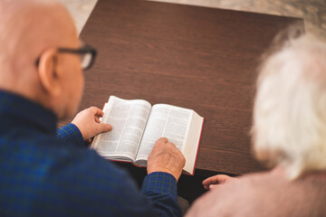 Elderly couple reading bible and pray together at home.