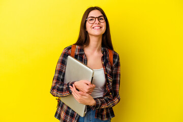 Young caucasian student woman holding a laptop isolated on pink background laughing and having fun.