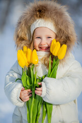 cute little girl in white winter clothes and a knitted hat walks in the winter forest with tulips. early spring, international women's day
