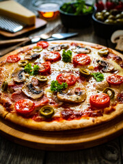 Pizza with champignons, ham, tomatoes, olives, parmesan and mozzarella  on wooden background
