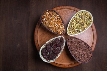 Top view of pistachio, chocolate, hazelnut and white chocolate stuffed easter eggs on a wooden stand.