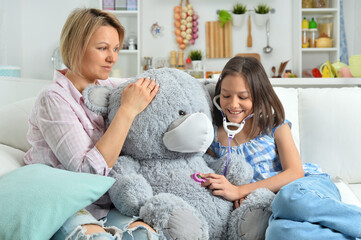  little girl and mother playing   with toy bear in facial mask. Girl with stethoscope