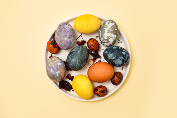Natural dye for Easter eggs. Homemade eggs are dyed with natural dyes, hibiscus tea, egg husks, turmeric. Colored Easter eggs, marble pattern. The background is yellow. Flat top view