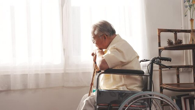 Elderly Senior male stay home after retirement alone at home unhappily and lonely his looking out the window with wheelchair and cane.