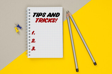 On a yellow-gray background are pencils, buttons and a notebook in which it is written - Tips And Tricks