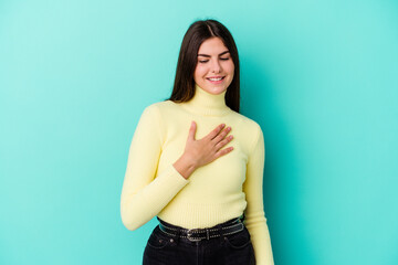 Young caucasian woman isolated on blue background laughing keeping hands on heart, concept of happiness.