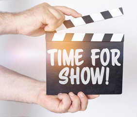 Obraz premium On a white background, a man holds a clapperboard in his hands on which it is written - TIME FOR SHOW