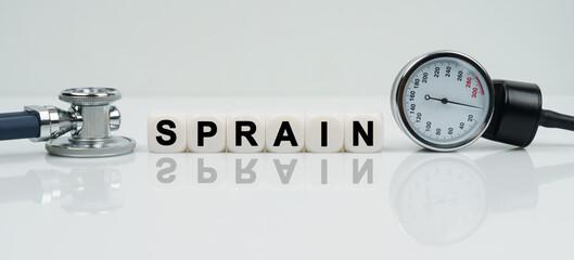 On a reflective white surface lies a stethoscope and cubes with the inscription - SPRAIN