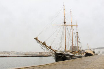 Obraz premium sailing ship with lowered sails moored on the embankment in rainy weather