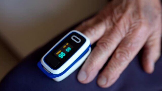 Old sick man measuring oxygen saturation level in blood with digital pulse oximeter at home, male patient with pneumonia monitoring oxygen rate by wearing oximeter on finger. Precautionary health care