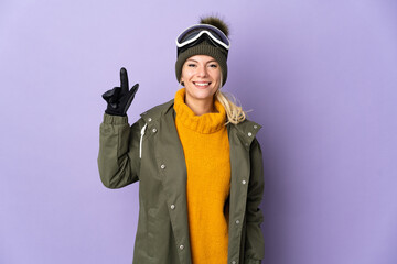 Skier Russian girl with snowboarding glasses isolated on purple background pointing up a great idea