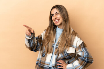 Fototapeta na wymiar Young caucasian woman isolated on beige background pointing finger to the side and presenting a product