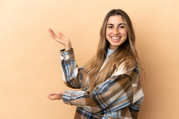 Young caucasian woman isolated on beige background extending hands to the side for inviting to come