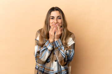 Young caucasian woman isolated on beige background happy and smiling covering mouth with hands