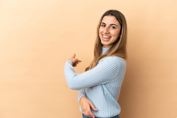 Obraz premium Young caucasian woman isolated on beige background pointing back