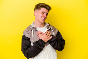 Young caucasian man isolated on yellow background has friendly expression, pressing palm to chest....