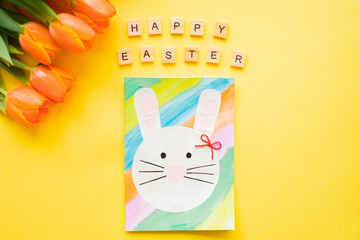 HAPPY EASTER text wooden letters and Hand-made Easter card and orange tulips on yellow background. Top view. Easter concept. 