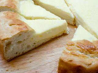 Close-up of triangular slices of sour cream pie - a national Tatar dish. A huge homemade cheesecake with toasted edges and tender filling on a wooden table.