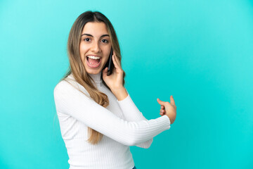 Fototapeta premium Young caucasian woman using mobile phone isolated on blue background pointing back