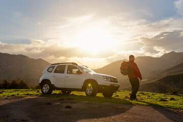 Hiker with backpack watches the sunset on the mountain with his all-terrain car. suv vehicle....