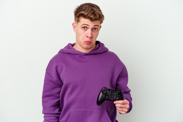 Young caucasian man holding a gamepad isolated on white background shrugs shoulders and open eyes confused.