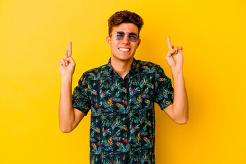 Young caucasian man wearing a Hawaiian shirt isolated on yellow background crossing fingers for having luck