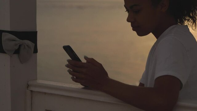 Young woman using mobile phone while watching sunrise on the seashore. Nature, technology, vacation concept