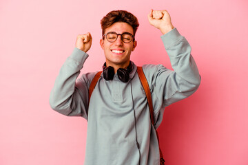 Young student man isolated on pink background celebrating a special day, jumps and raise arms with...