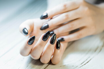 Gorgeous manicure, black nail polish with sequins, close-up photo. Women's hands on a simple...