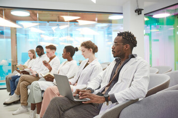 Multi-ethnic group of young people wearing lab coats and taking notes while sitting in during lecture on medicine in college, copy space