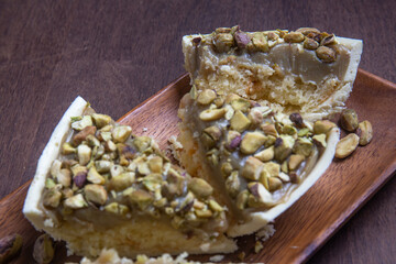 Cracked stuffed pistachio and white chocolate easter egg on a wooden stand on a wooden table.