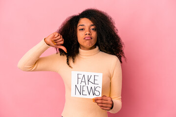 Young african american curly woman holding a fake news on a placard showing a dislike gesture, thumbs down. Disagreement concept.