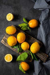 Fresh ripe yellow lemon fruits with leaves and fabric on dark stone background